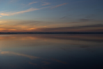 Muted sunrise over still lake with soft pastel sky reflections.