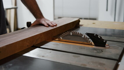 A craftsman carefully pushes a thick wooden board through a spinning.