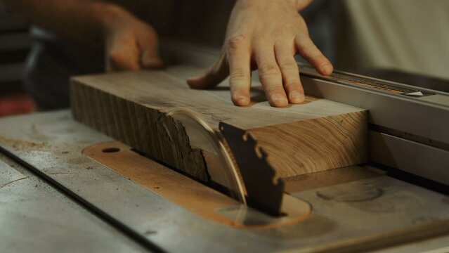 Close up view of a craftsman cutting a wooden plank with a table saw
