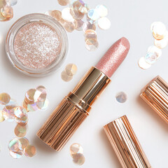 Luxurious gold and rose gold cosmetic products arranged with iridescent confetti for a celebratory beauty campaign.
