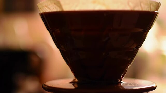 Close-up coffee dripper with filter, brewing coffee, in a warm, out-of-focus cafe setting. Use coffee shop imagery