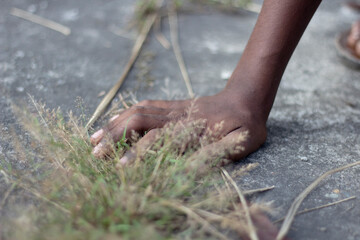 Closeup of a darkskinned persons foot touching dry grass on concrete