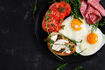 English breakfast. Fried eggs, salami, tomatoes and toast with feta and pesto. Top view.