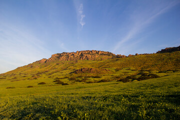 Sunlit green hillside and rugged rock formations under blue sky