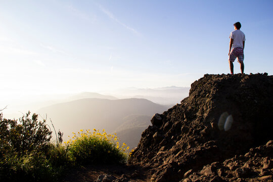 Man on rocky summit gazing at sunlit misty mountain landscape