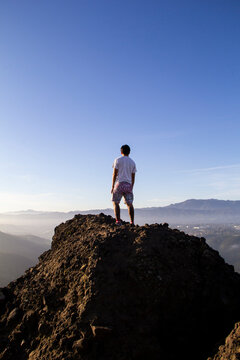 Man standing on rocky peak overlooking hazy mountains at sunrise
