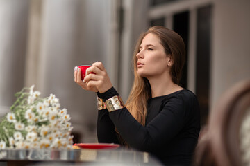 Woman Coffee Daisies: Contemplative woman drinks coffee outside during daytime, enjoying flowers.