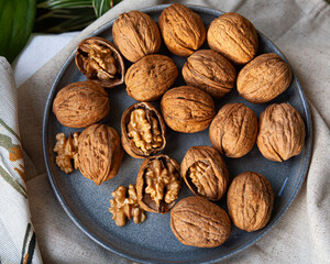 Fresh walnuts in shell on a rustic plate — some cracked to reveal creamy kernels. Natural, healthy snack.