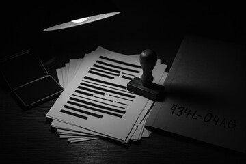 Redacted document with black bars and wooden stamp on desk under lamp, dramatic lighting conveys secrecy and tension