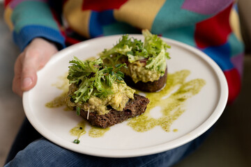 Man eating healthy avocado toast with greens on rye bread