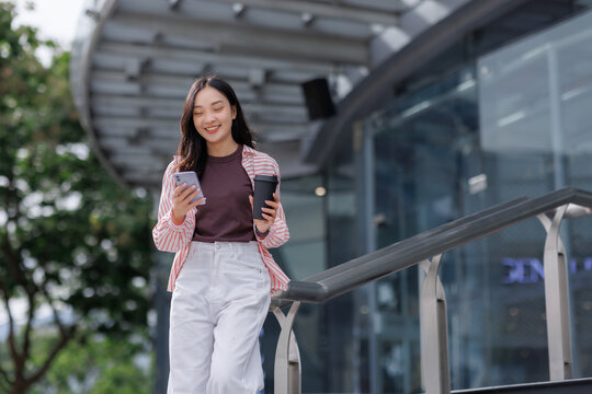 Young woman walking outdoors using smartphone and drinking coffee