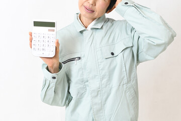 電卓を持ちながら困る作業服姿の中高年女性
