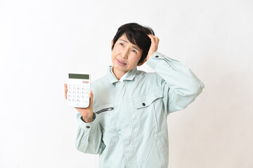 電卓を持ちながら困る作業服姿の中高年女性
