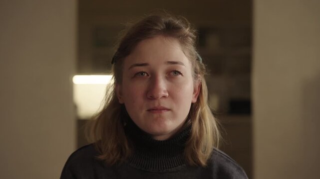 Portrait of serious young woman with cerebral palsy and strabismus looking up, showing candid portrait of disability, representing human experience and diverse representation in everyday life.