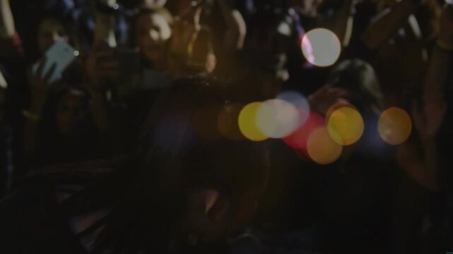 Singer stepping on concert stage starting singing into mic as phone lights energizing crowd