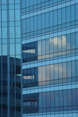 Obraz premium Modern Blue Glass Skyscraper Facade with Dynamic Reflections and Geometric Grid.