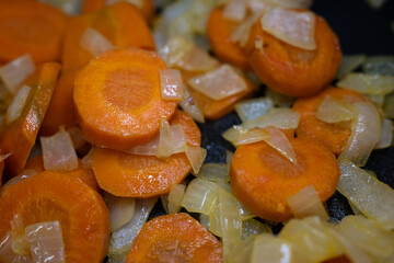 Close-up of fresh sliced carrots and chopped onions sautéing in a pan. Vibrant, healthy vegetables for cooking concepts, meal prep, and delicious homemade food.