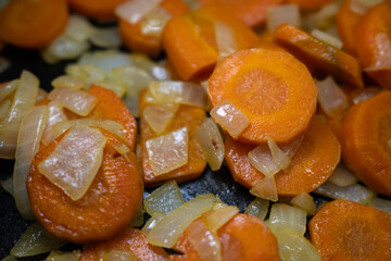 Close-up of fresh sliced carrots and chopped onions sautéing in a pan. Vibrant, healthy vegetables for cooking concepts, meal prep, and delicious homemade food.