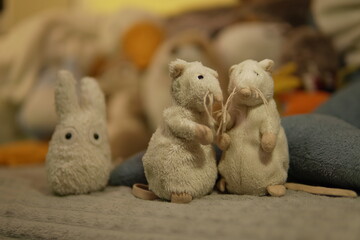 Two small gray plush mice (or hamsters) standing next to a plush rabbit against a blurred...