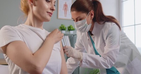 Nurse or doctor giving injection to female patient in clinic to prevent pandemic. Woman receiving a dose of vaccine in medical center or hospital. Vaccination and medicine concept. 4k video. - Powered by Adobe