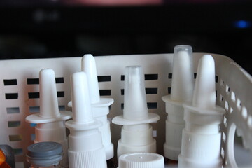 Assorted white nasal spray bottles stored in a small plastic basket. Medical supplies for cold relief, allergies, sinus treatment and home pharmacy organization.