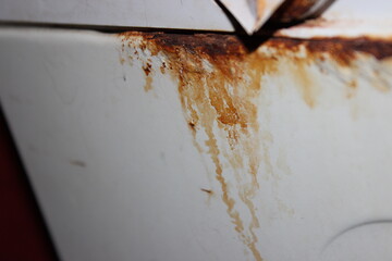Close-up of rust and corrosion stains on a white metal surface, showing heavy oxidation and...