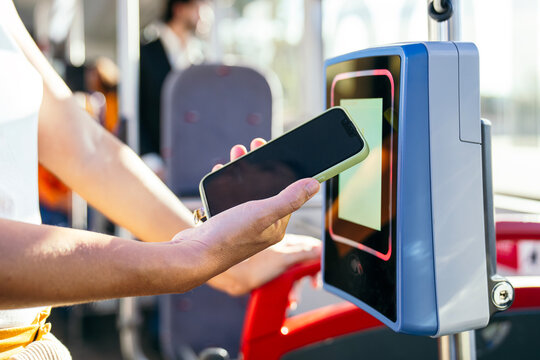 Woman using mobile payment on a contactless reader inside a public city bus, representing modern travel and technology