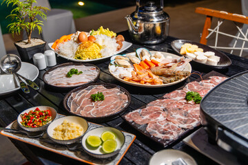 Gourmet seafood and meat platter with fresh ingredients on outdoor table, ideal for barbecue. Features shrimp, mussels, sliced meat, vegetables, and condiments in vibrant setting.