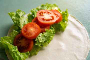 Fresh lettuce and tomato atop tortilla for healthy wrap