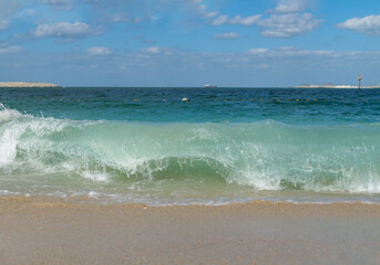 Bright blue sea waves crashing on the sandy shore under a clear sky in a coastal location .