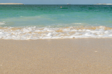 Bright blue sea waves crashing on the sandy shore under a clear sky in a coastal location .
