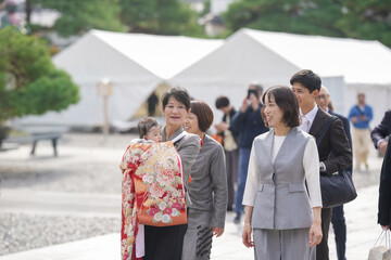 A group of people are walking down a street, with a woman wearing a red and white outfit carrying a baby