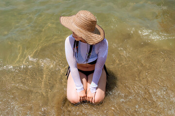 Woven shade and waterlight — woman seated in Caribbean shallows at Covenhas.