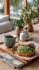 A Healthy Vegan Sandwich with Sliced Avocado and Sesame Seeds Served on a Wooden Board with a Cup of Coffee and a Napkin on a Table Near a Window with Green Plants