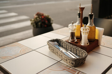 Neatly arranged dining table with olive oil bottles, condiments, and metal cutlery in wicker basket