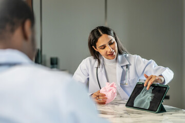 Two cardiologists engage in a detailed discussion on heart disease treatment, using an anatomical model to illustrate their points while consulting with a medical doctor in a clinic, share knowledge