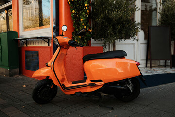 Bright orange scooter standing by vivid urban facade with plants and decorative lemons