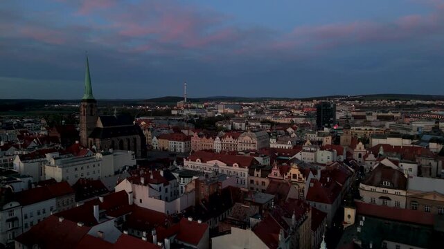 Low altitude aerial drone shot flying over colorful historic Pilsen rooftops towards Republic Square and the Gothic Cathedral of St. Bartholomew at dusk.