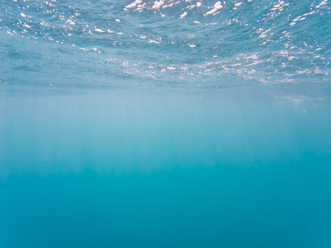 Serene underwater background of clear blue ocean water with sunlight rays shimmering through the surface.