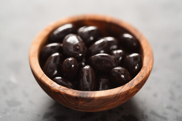 Dark chocolate dragee in olive wood bowl on concrete background