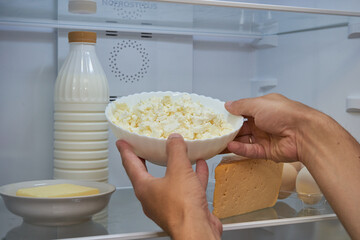 male hands take sour milk cheese from the refrigerator, A man takes some homemade cheese from a plate in an open refrigerator.