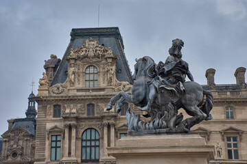 Obraz premium Equestrian statue of Louis XIV in the courtyard of the Louvre Museum in Paris with a cloudy sky and classical architecture in the background
