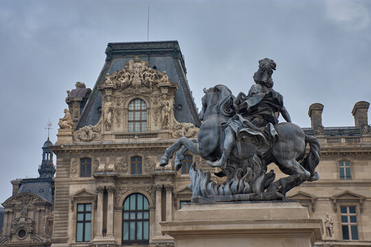 Equestrian statue of Louis XIV in the courtyard of the Louvre Museum in Paris with a cloudy sky and classical architecture in the background