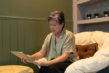 An elderly woman is comfortably using a tablet while enjoying her cozy indoor environment