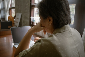 Asian elder woman sitting with laptop in  Warm and Cozy Workspace, Perfect for Inspiring Deep Thoughts and Ideas