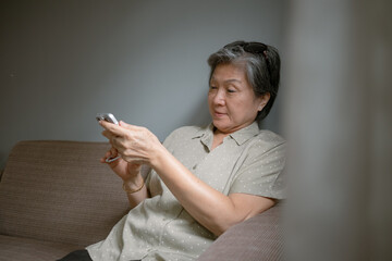 Asian Thai Engaged Senior Woman Using Her Smartphone While Relaxing in a Cozy Home Environment.