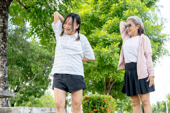 Asian senior woman stand and guide to her friend to stretching arm and shoulder in the garden wiith day light.