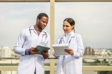 Latin female doctor talking with African American male colleague during work break rooftop of the hospital. Friendly conversation between two doctors during a lunch break of a clinic