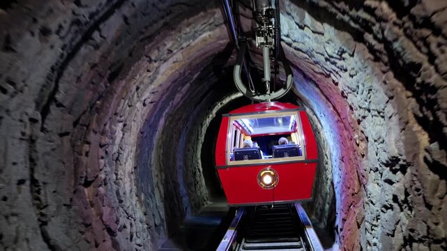 A dynamic video shot from a low angle captures a red funicular in a stone tunnel, highlighting its vibrant colors and unique underground setting.