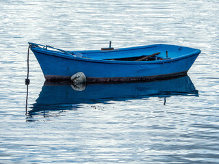 Naklejka premium Barca de pesca de color azul intenso amarrada en medio del mar en calma